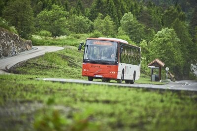 Bilde av en orange og hvit buss som kjører en svingete vei, omgitt av grønn vegetasjon